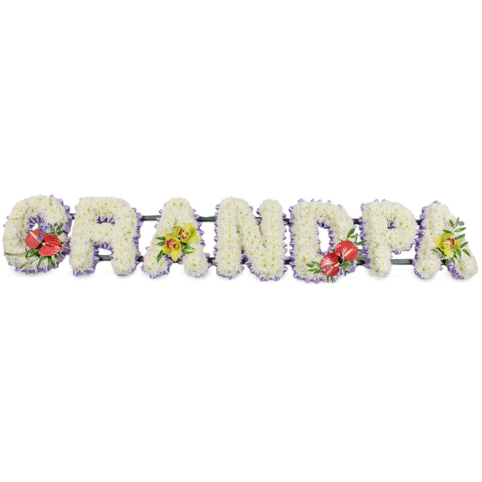 Here, the word "GRANDPA" stretches horizontally across the frame, each letter rendered in bold, three-dimensional capitals and crafted entirely from fresh white chrysanthemums. Against a clean white background, the flowers seem to glow softly, each small bloom pressed closely to its neighbours to form dense, rounded cushions. The uniform white petals create a sense of purity and quiet, the sort of calm presence that offers comfort at a funeral or celebration of life. A trim of pale lavender ribbon runs along the lower edge of each letter, a light purple band that subtly outlines the shapes and adds a cool, calming contrast without overwhelming the purity of the design. The letters are attached to a dark green metal base, the supporting bars linking them together in a continuous line, ready to rest beside a coffin or at the front of a service in De Beauvoir Town, perhaps in a local church off De Beauvoir Road or in a small funeral home near Regent's Canal. Colour and character are introduced through four accent clusters. On the "G" and "D," deep red anthuriums with their wax-like, heart-shaped faces and striking yellow spadices burst from gatherings of rich foliage and delicate purple filler blooms, their intensity suggesting strong affection and vivid memories. On the first and last "A," sprays of yellow-green orchids are arranged with care, their arching stems and intricate petals lending refinement and hinting at life that continues in memory. It feels like a thoughtfully designed tribute from De Beauvoir Town Florist, created for a family who want to honour their grandfather with flowers that express love, pride, and gratitude in a simple, eloquent way.